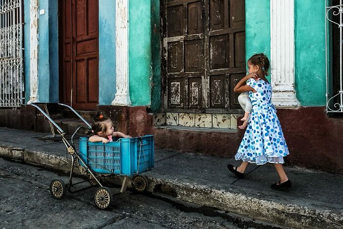 Two young girls share a tender moment on a vibrant street, captured in a candid street photo showcasing humanity and everyday life.