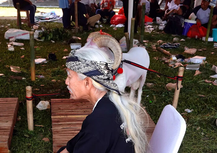 Elderly man with long white hair and horned headband in a street scene captured with perfect timing by photographer.