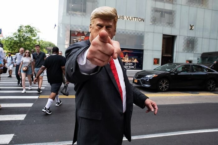 Man in a suit and red tie pointing at the camera on a busy city street, capturing a candid street photo moment.