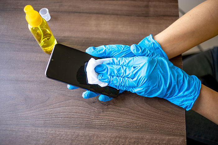 Person wearing blue gloves wiping smartphone screen with cloth and spray bottle, hygiene mistakes
