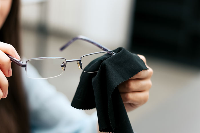 Hands cleaning eyeglasses with a cloth, illustrating hygiene mistakes in lens care