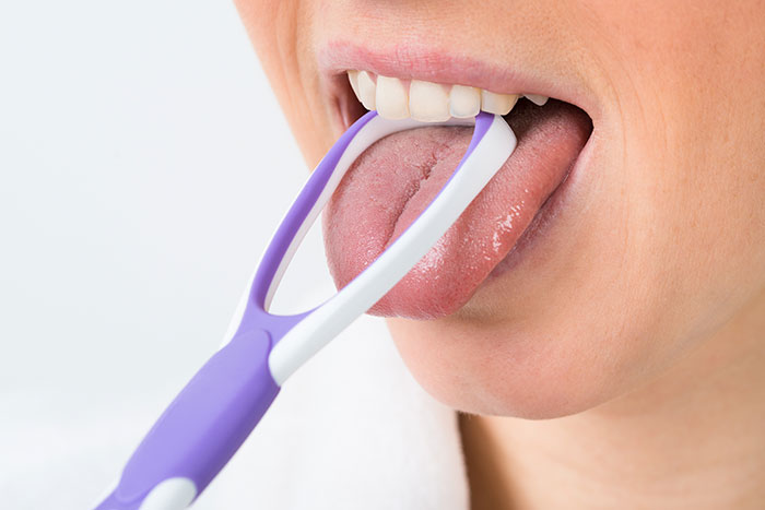 Adult using purple tongue scraper to clean tongue, hygiene mistakes adults example