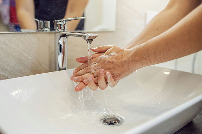 Person washing hands at a sink, representing hygiene mistakes adults make