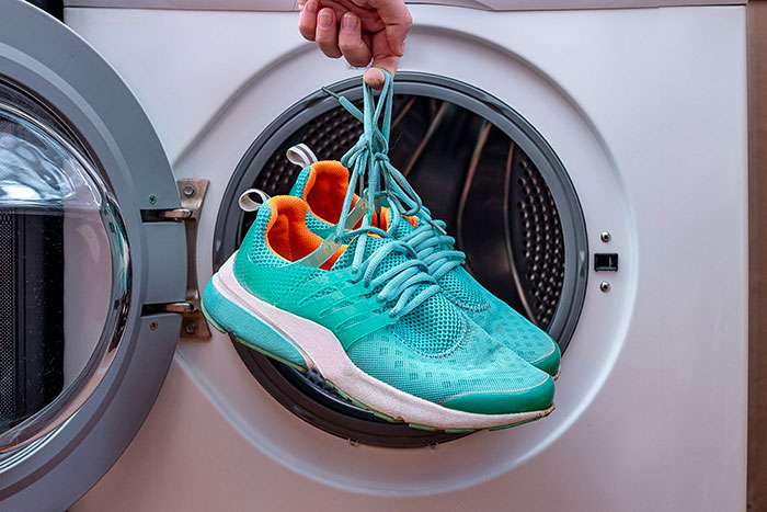 Turquoise running shoes held by laces in a washing machine drum, illustrating hygiene mistakes.