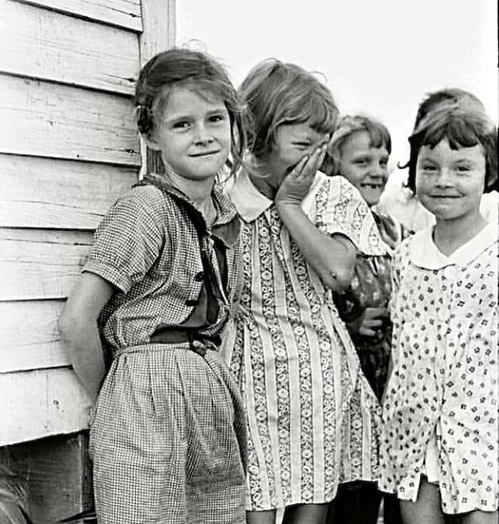 Group of young girls smiling and laughing outside a wooden building, capturing a moment in the history of humanity.