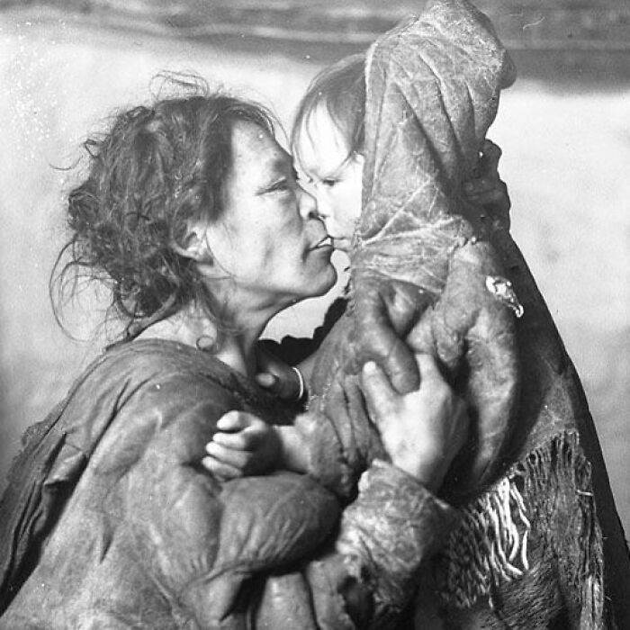 Black and white photograph of a mother holding and kissing her child, depicting the sad, beautiful history of humanity.
