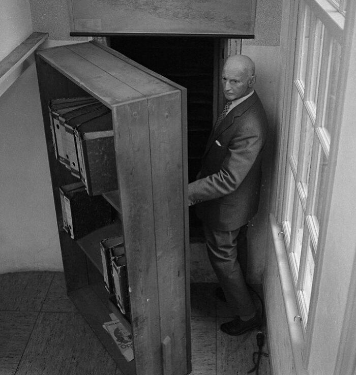 Man in suit opening secret bookshelf door in a narrow hallway, capturing a unique moment in the history of humanity.