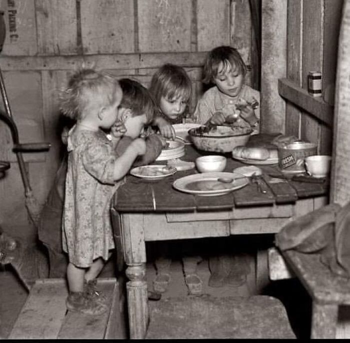 Four children eating modest food around a wooden table, capturing a sad and beautiful moment in history of humanity.