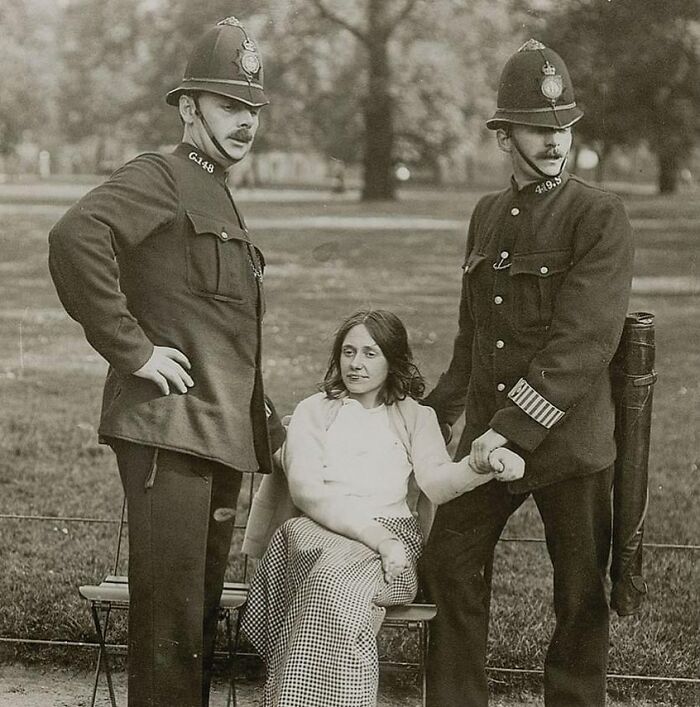 Black and white historic photograph showing police officers escorting a distressed woman, capturing history of humanity moments.