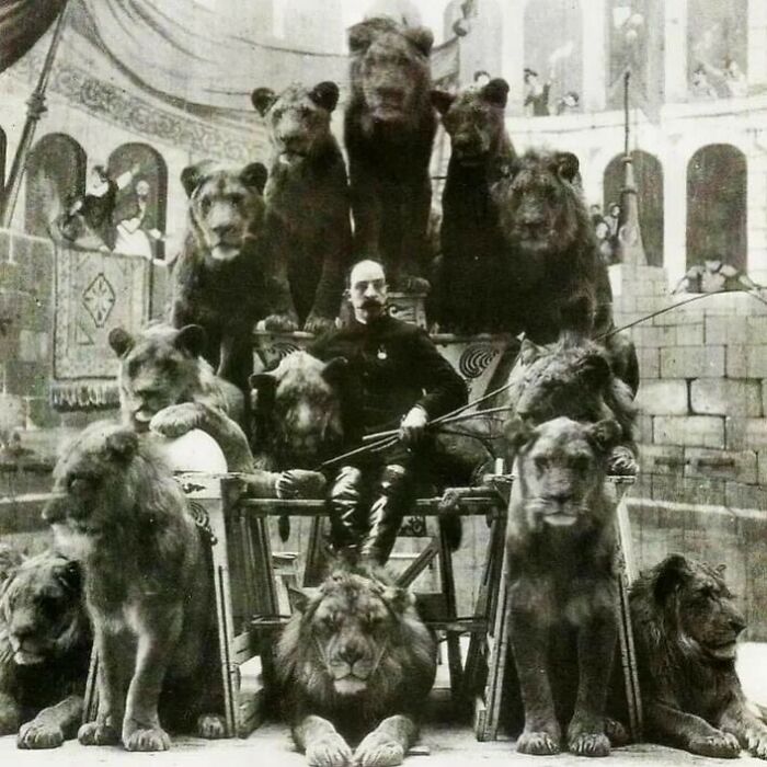 Man seated among multiple lions and bears in a historic black and white photograph showing the history of humanity.