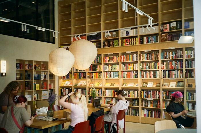 People in a cozy library setting, surrounded by bookshelves, engaged in quiet activities behind the scenes.