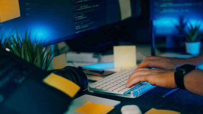 Person typing on a keyboard in a dimly lit office, showing behind scenes of people in boring industries work.