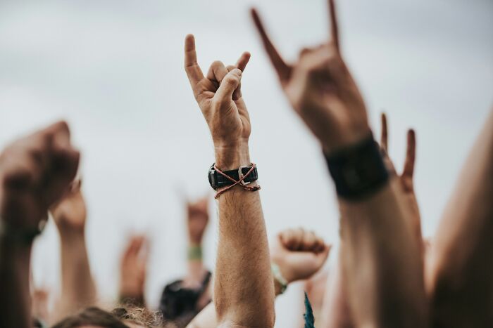 Raised hands showing rock or horn gestures at a crowded event illustrating things normal in America but offensive elsewhere.