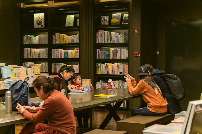 People in a quiet library setting, engaging with books and devices, showing behind scenes of boring industries.