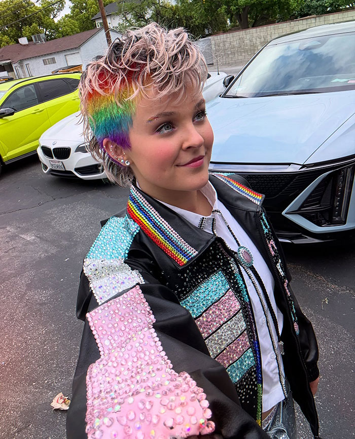 JoJo Siwa with a rainbow hairstyle and colorful studded jacket showcasing her massive transformation and bold new look outdoors. JoJo Siwa with a rainbow hairstyle and colorful studded jacket showcasing her massive transformation and bold new look outdoors.