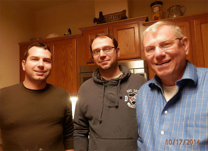 Three men standing in a kitchen, with the father of ICE agent who slew Renee Nicole Good smiling in a blue shirt. Three men standing in a kitchen, with the father of ICE agent who slew Renee Nicole Good smiling in a blue shirt.