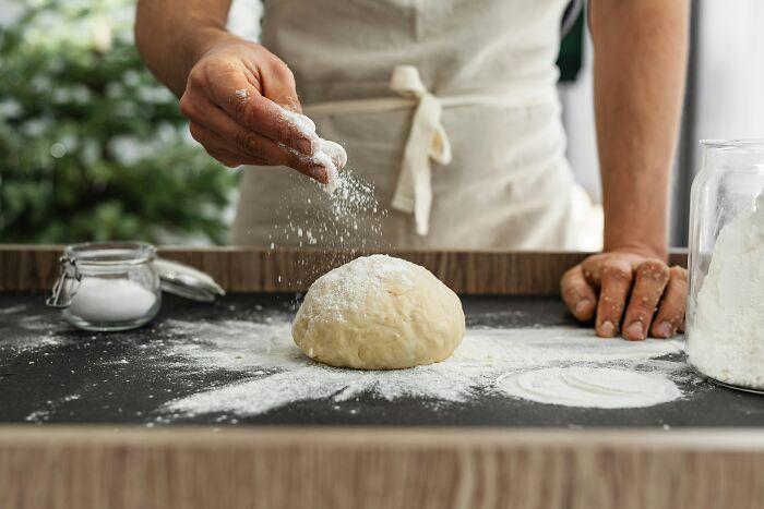 Person sprinkling flour on dough on a kitchen counter, illustrating a metaphor for worst coworkers making work feel like a nightmare.