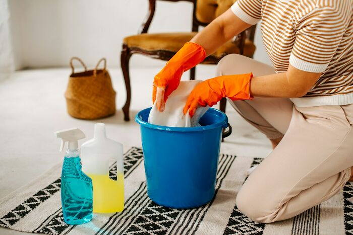 Person wearing orange gloves preparing cleaning solution in a blue bucket, highlighting daily dangers from household chemicals.