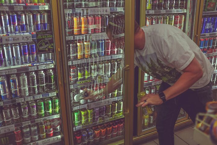 Man selecting energy drinks from a refrigerated display, highlighting daily dangers you might not realize you’re exposed to.