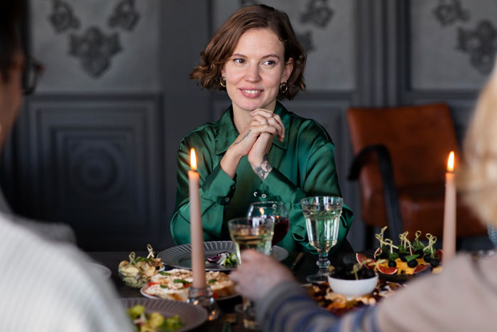 Woman in green shirt at dinner table with candles and appetizers, illustrating family tensions over wedding planner issues.