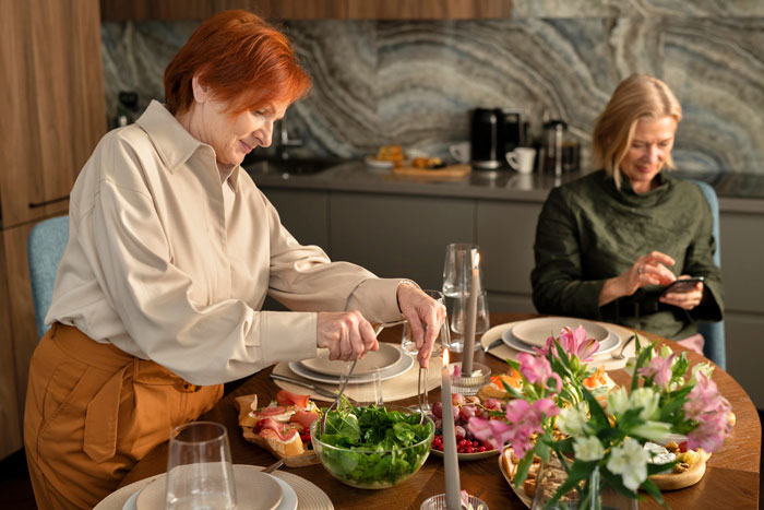 Two women at a dining table with food, illustrating family conflict involving a MIL and wedding planner controversy.