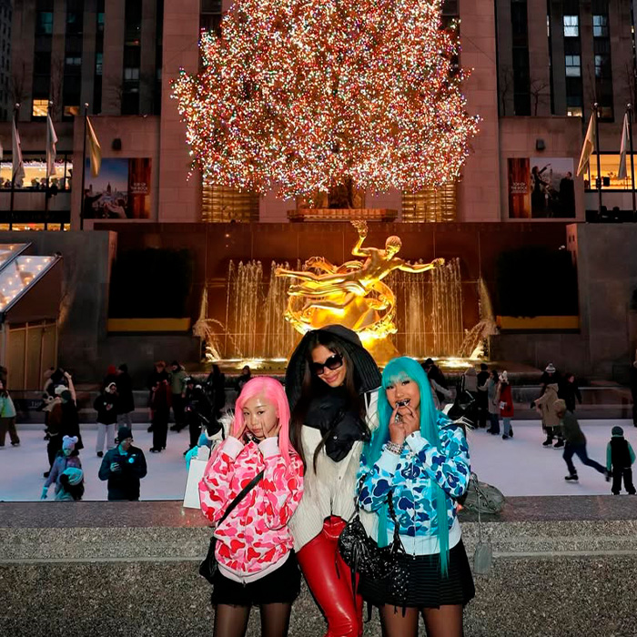 Three women posing in front of an illuminated Christmas tree and fountain, highlighting Kim Kardashian and North West interaction.