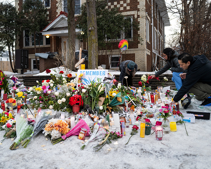 People placing flowers and candles at a memorial site in Minneapolis after ICE slaying, reflecting public outrage and grief.