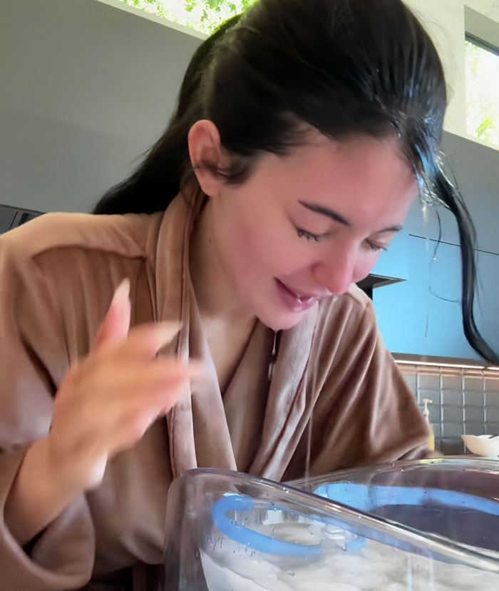 Woman in a bathrobe demonstrating a beauty hack related to Botox treatment in a modern bathroom setting.