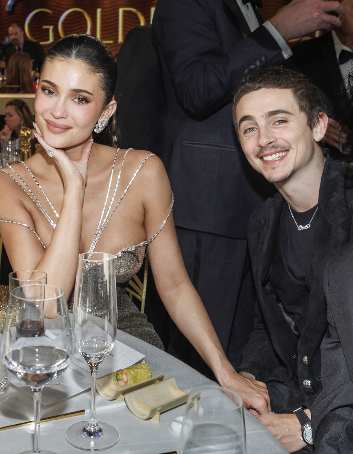 Kylie Jenner at Golden Globes seated at table with drinks and holding hands with a smiling man during event. Kylie Jenner at Golden Globes seated at table with drinks and holding hands with a smiling man during event.