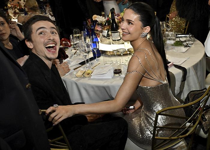 Kylie Jenner seated at Golden Globes event wearing shimmering dress, sparking a heated debate online about her seat photo.