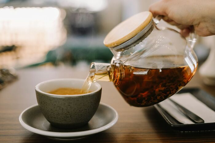 Pouring tea from a glass teapot into a cup, illustrating a cultural norm in America but offensive elsewhere.