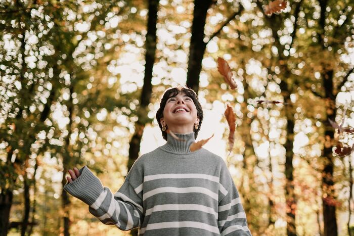 Person enjoying autumn outdoors, smiling and tossing leaves in a forest, illustrating adult goals and lifestyle.