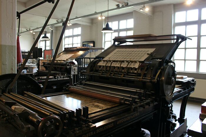 Vintage industrial printing machines in a bright workshop showing people working in boring industries behind the scenes.