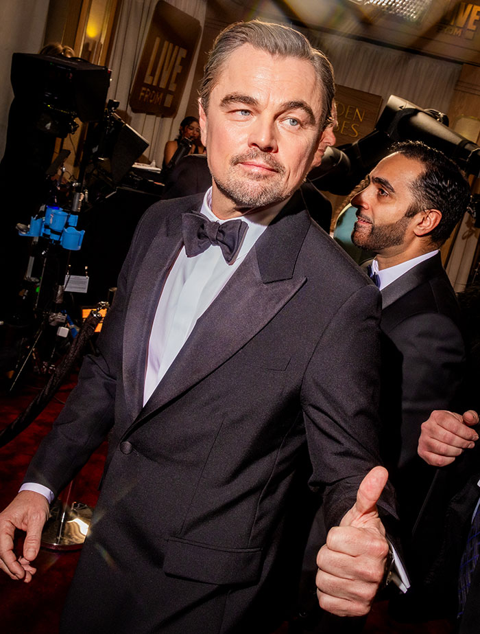 Leonardo DiCaprio on the red carpet at the Golden Globes in a tuxedo, with a confident and sassy expression.