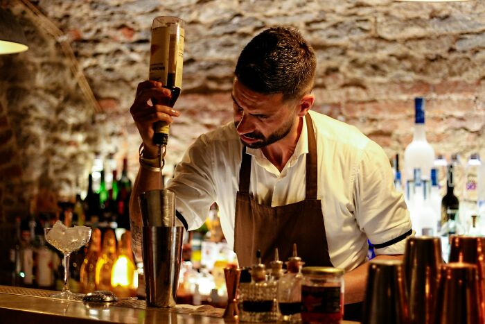 Bartender pouring alcohol into a shaker in a dimly lit bar, showcasing a weird public behavior with zero shame.