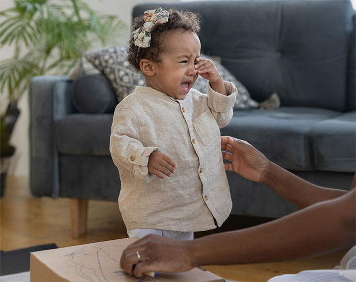 Crying 3-year-old toddler upset after being disciplined by grandparents in a living room setting.