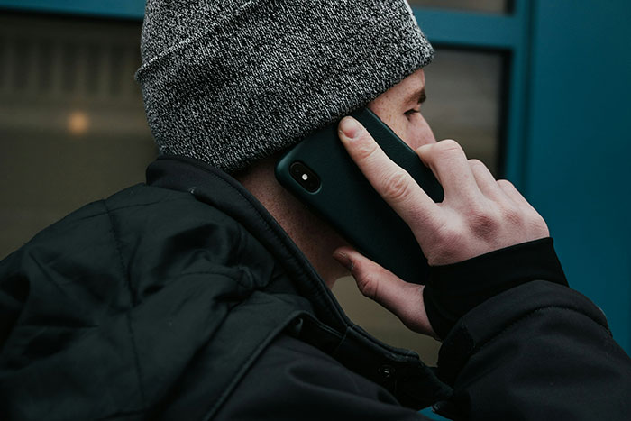 Man wearing a gray beanie talking on phone, depicting family forgiveness and tension over past beating incident.