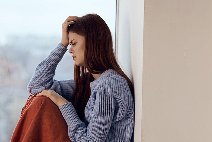 Young woman in a blue sweater sitting alone, looking upset after man shows his true colors assuming fianc&eacute;e is pregnant.