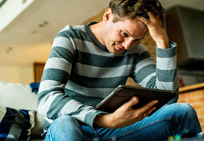 Man sitting in his apartment looking worried while holding a tablet, noticing strange things happening around him. Man sitting in his apartment looking worried while holding a tablet, noticing strange things happening around him.