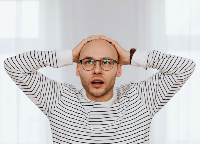 Stressed bald man wearing glasses and striped shirt, holding head in disbelief, representing unemployed and jobless struggles. Stressed bald man wearing glasses and striped shirt, holding head in disbelief, representing unemployed and jobless struggles.