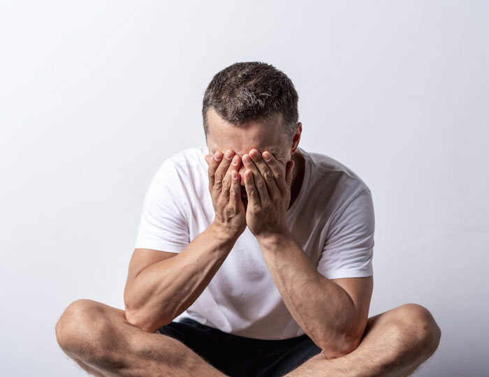 Man in a white shirt sitting cross-legged with face buried in hands, conveying distress and unemployment emotions. Man in a white shirt sitting cross-legged with face buried in hands, conveying distress and unemployment emotions.
