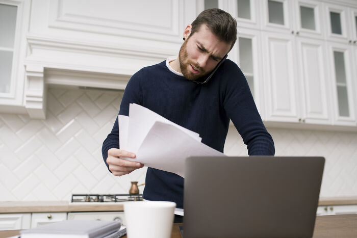 Man multitasking with phone and papers, appearing stressed during petty fights among couples over Christmas period.