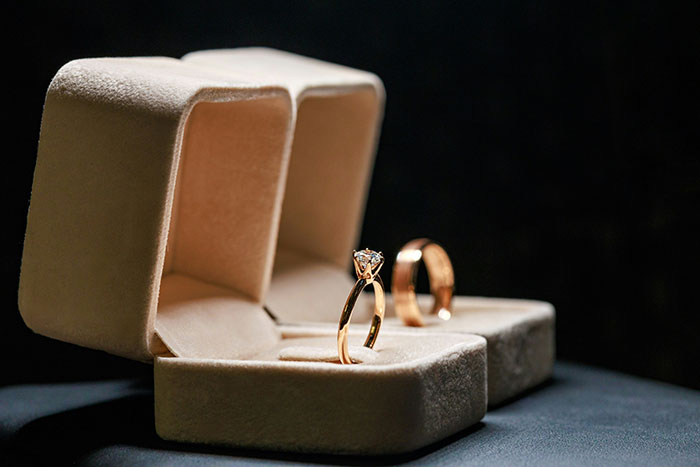 Close-up of gold rings in velvet boxes symbolizing reckoning and revenge in a dramatic, dark setting.