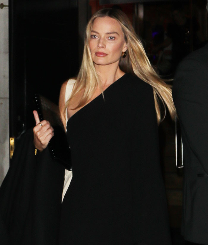 Margot Robbie in a black outfit walking at night, related to her underwater cover shoot brutally roasted online.