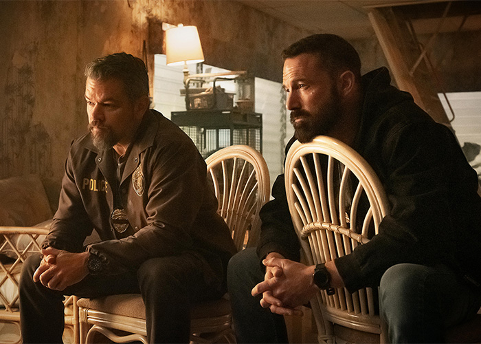 Two men sitting on wicker chairs in a dimly lit room, with serious expressions and casual dark clothing. Two men sitting on wicker chairs in a dimly lit room, with serious expressions and casual dark clothing.