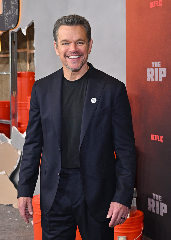 Matt Damon smiling at a red carpet event, wearing a black suit and posing against a promotional backdrop. Matt Damon smiling at a red carpet event, wearing a black suit and posing against a promotional backdrop.