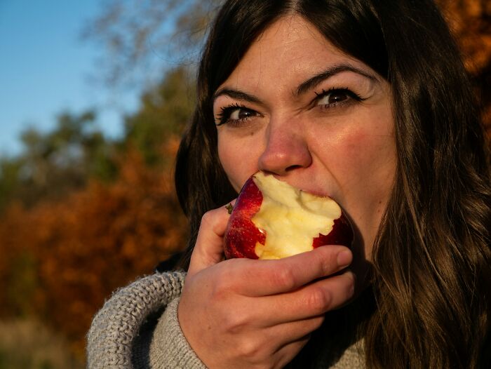 Woman biting into an apple outdoors, illustrating one of the daily dangers you might not realize exposing yourself to.