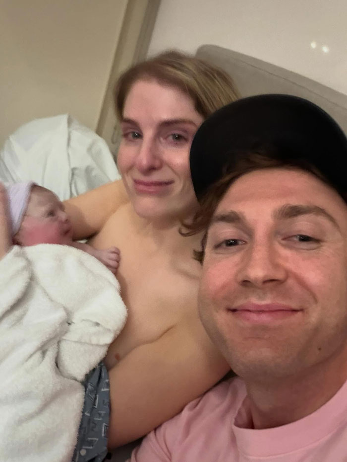 New parents smiling with their newborn wrapped in a blanket in a hospital room, highlighting surrogate baby news. New parents smiling with their newborn wrapped in a blanket in a hospital room, highlighting surrogate baby news.