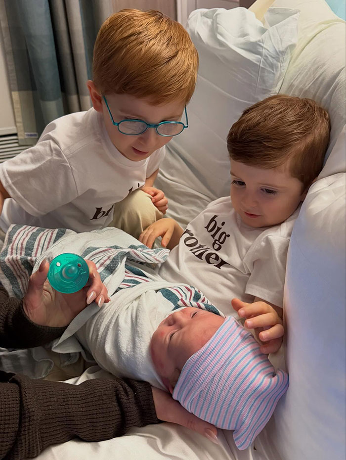 Two young boys wearing big brother shirts look at a newborn baby in a hospital bed with a secret surrogate baby theme. Two young boys wearing big brother shirts look at a newborn baby in a hospital bed with a secret surrogate baby theme.