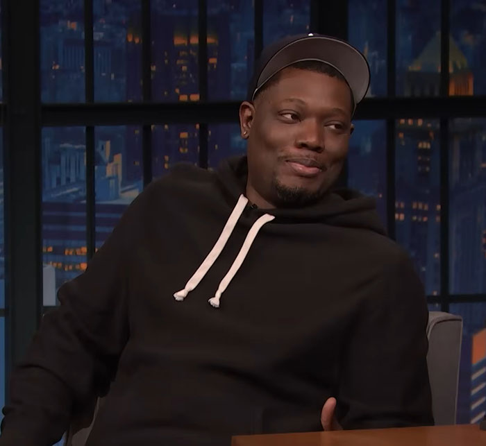 Michael Che on SNL wearing a black hoodie and cap, sparking heated debate with a joke about ICE on Weekend Update.
